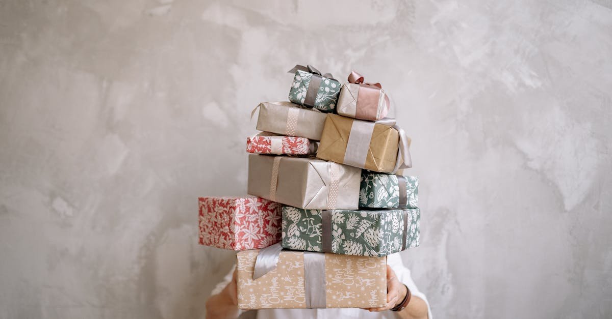 Person hiding behind a tall stack of gift-wrapped boxes against a gray wall, indoors.